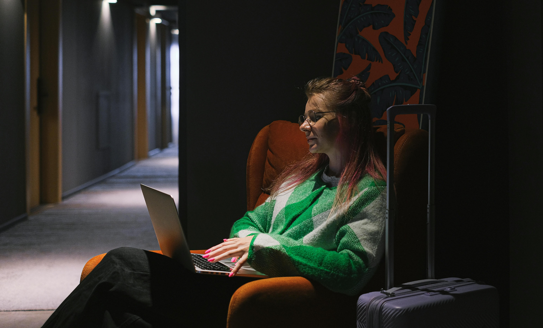 Kvinna sitter i stol med laptop bredvid sitt bagage